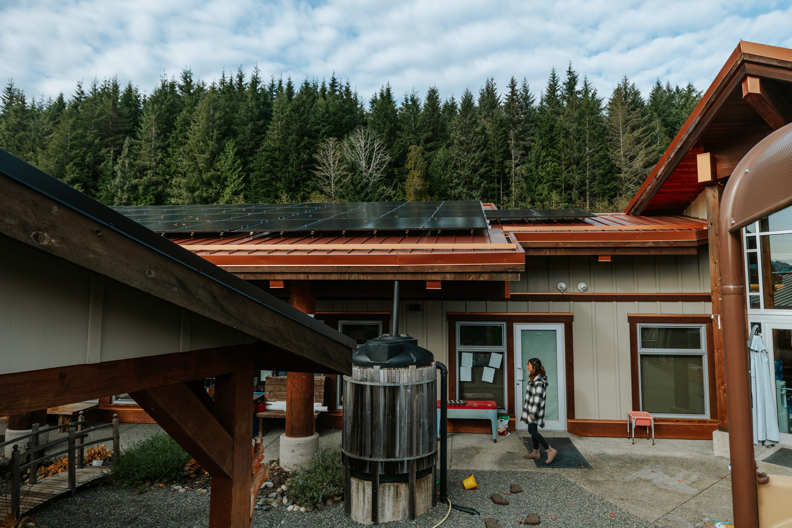 Kara Wilson walks through a courtyard at Quatsino daycare, solar panels visible on the roof above her.
