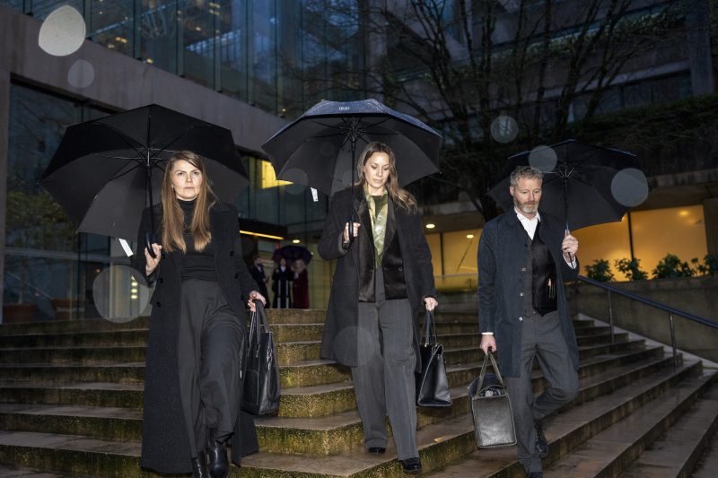 Amber Bracken, Carol Linnitt and Sean Hern hold black umbrellas walk toward the camera down a small flight of stairs.