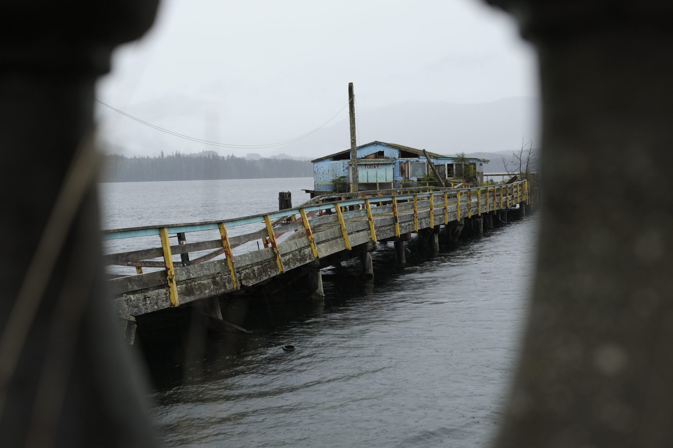 A collapsing dock over the ocean, with a small building at the end bearing a sign that says "Today"