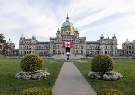 A view of the front lawn of the BC legislature with a large Canadian Flag hanging above the front steps