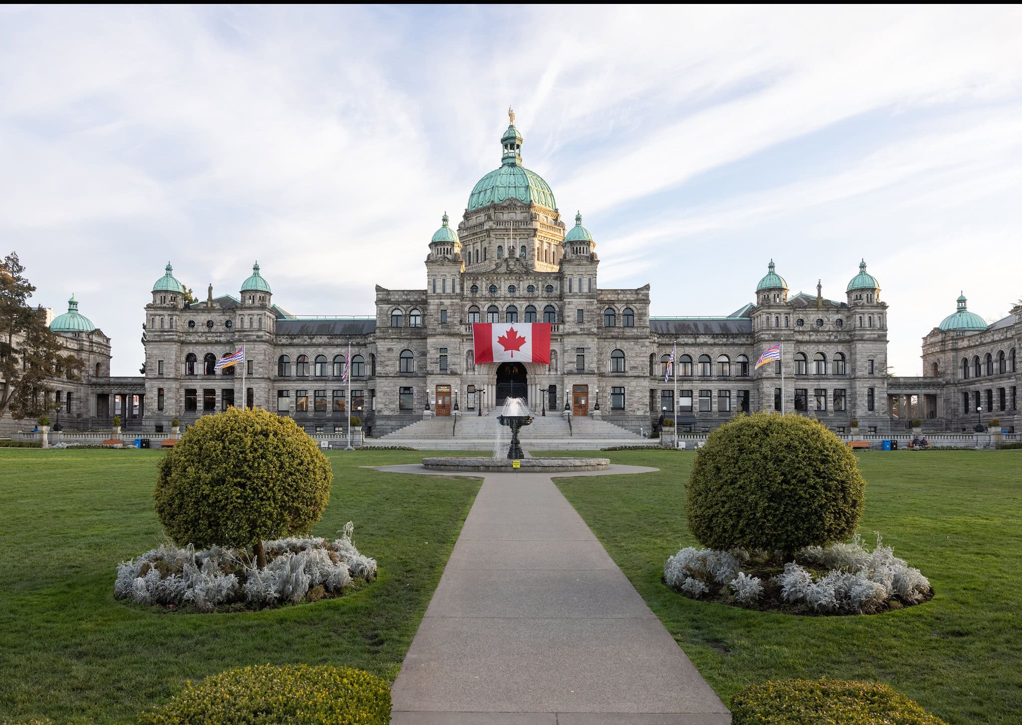 A view of the front lawn of the BC legislature with a large Canadian Flag hanging above the front steps
