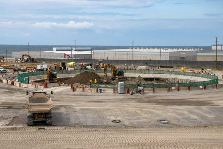 Heavy machinery operates in a construction site, where a low concrete wall surrounds a large circular hole in the ground