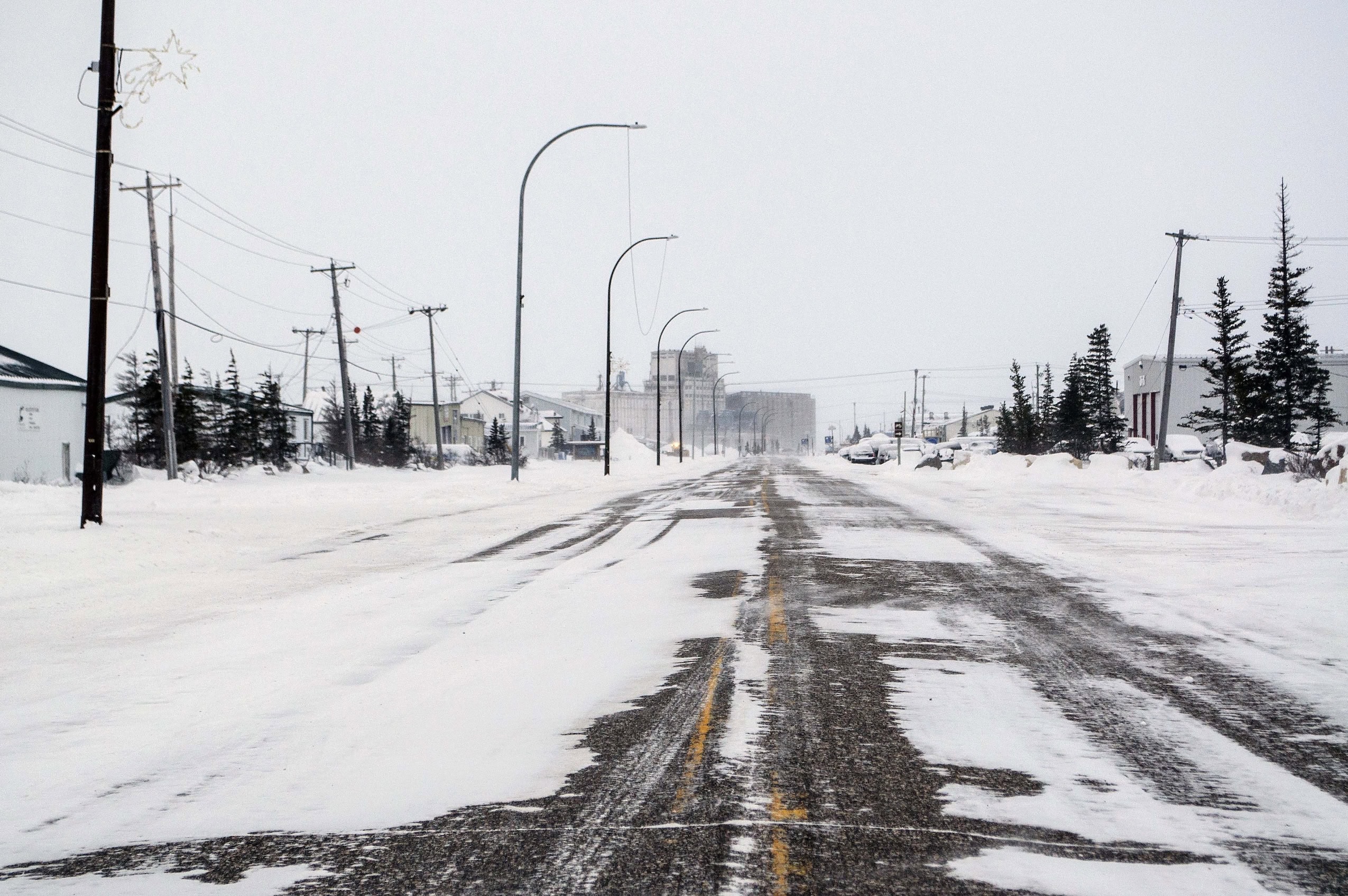 A snow and ice-covered road in an Arctic landscape, with an airport building in the far distance.