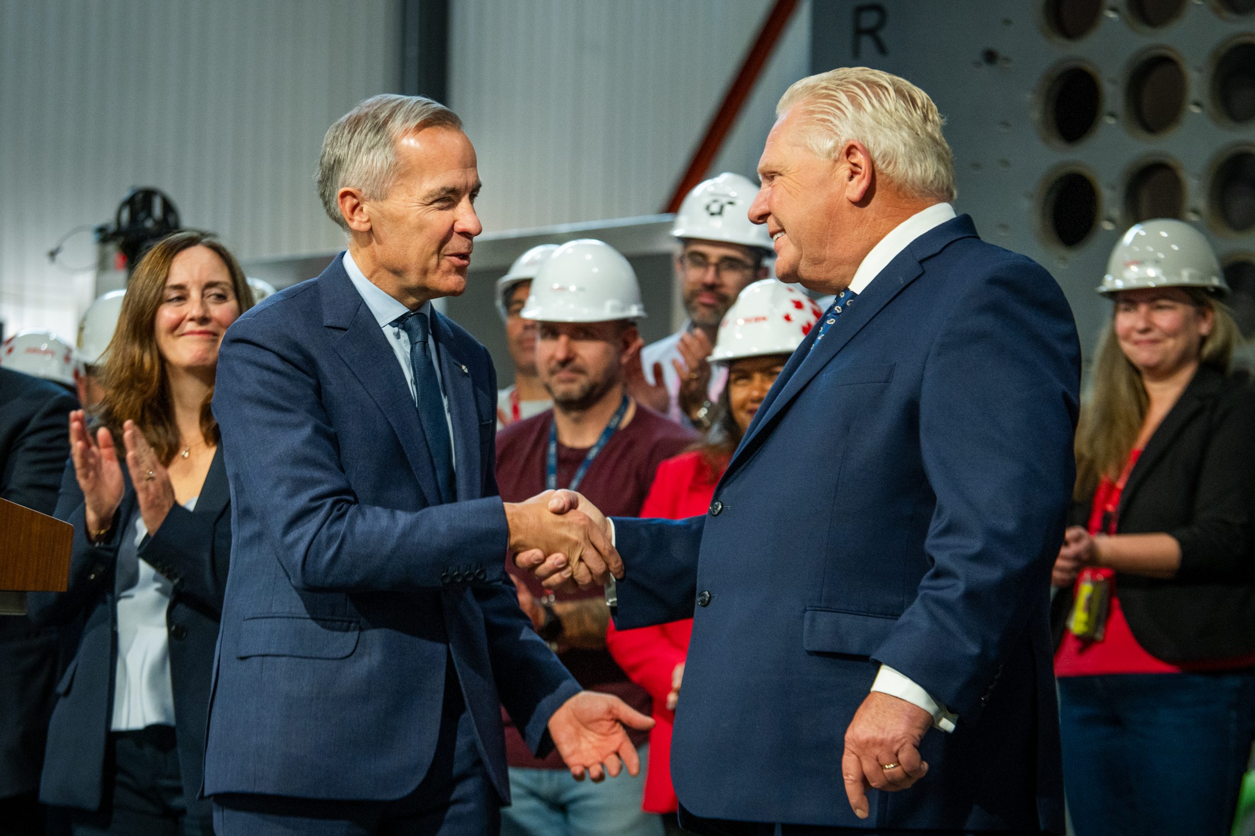 Prime Minister Mark Carney, left, shakes hands with Ontario Premier Doug Ford as people wearing hard hats in a nuclear facility watch on