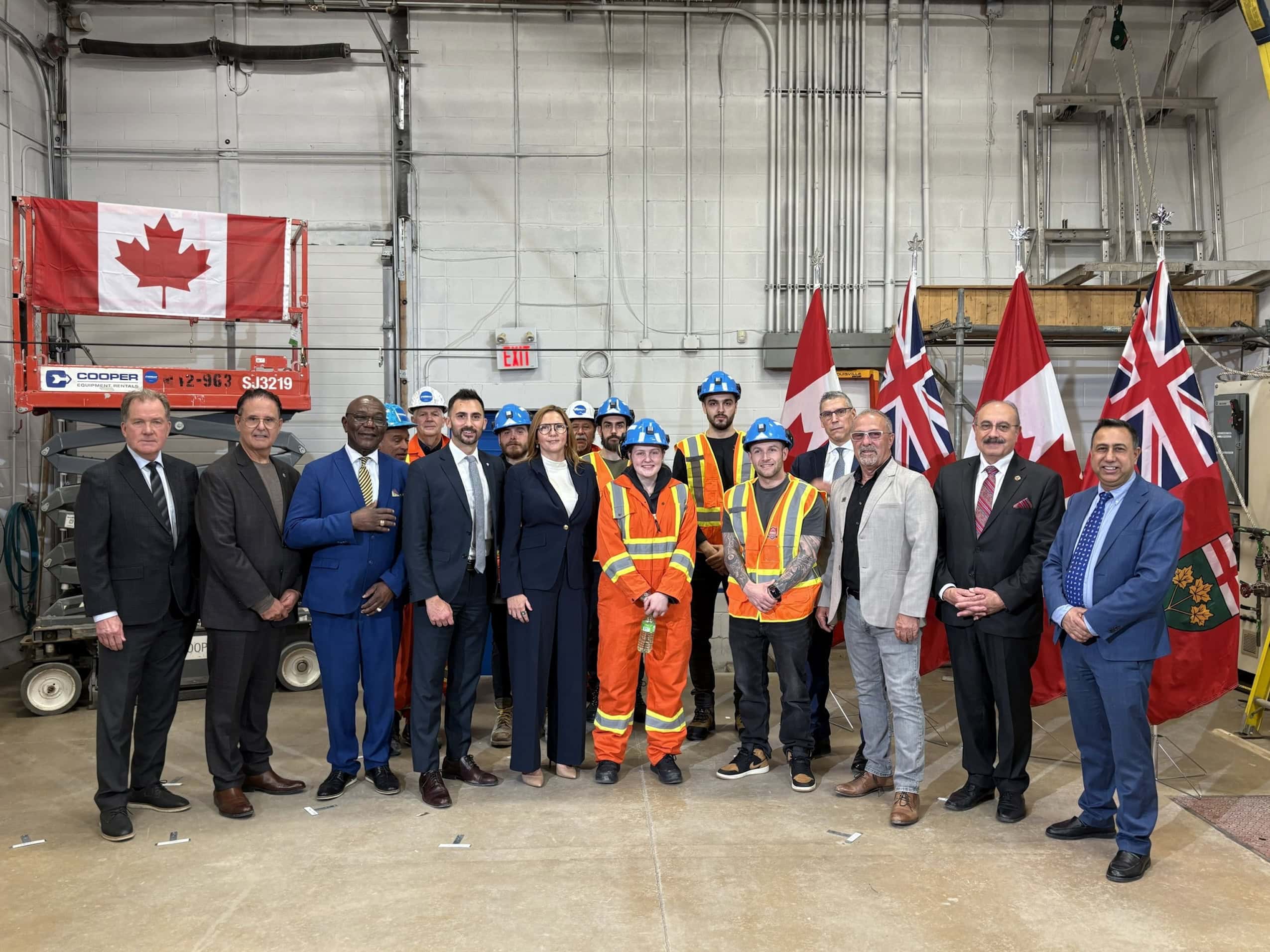 Politicians, mining executives and workers in hard hats pose in front of Canadian and Ontario flags.