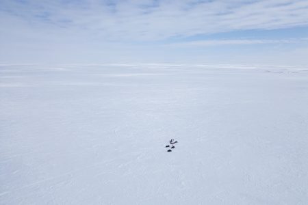 An aerial view of a handful of people dwarfed by a vast Arctic landscape dominated by sea ice.