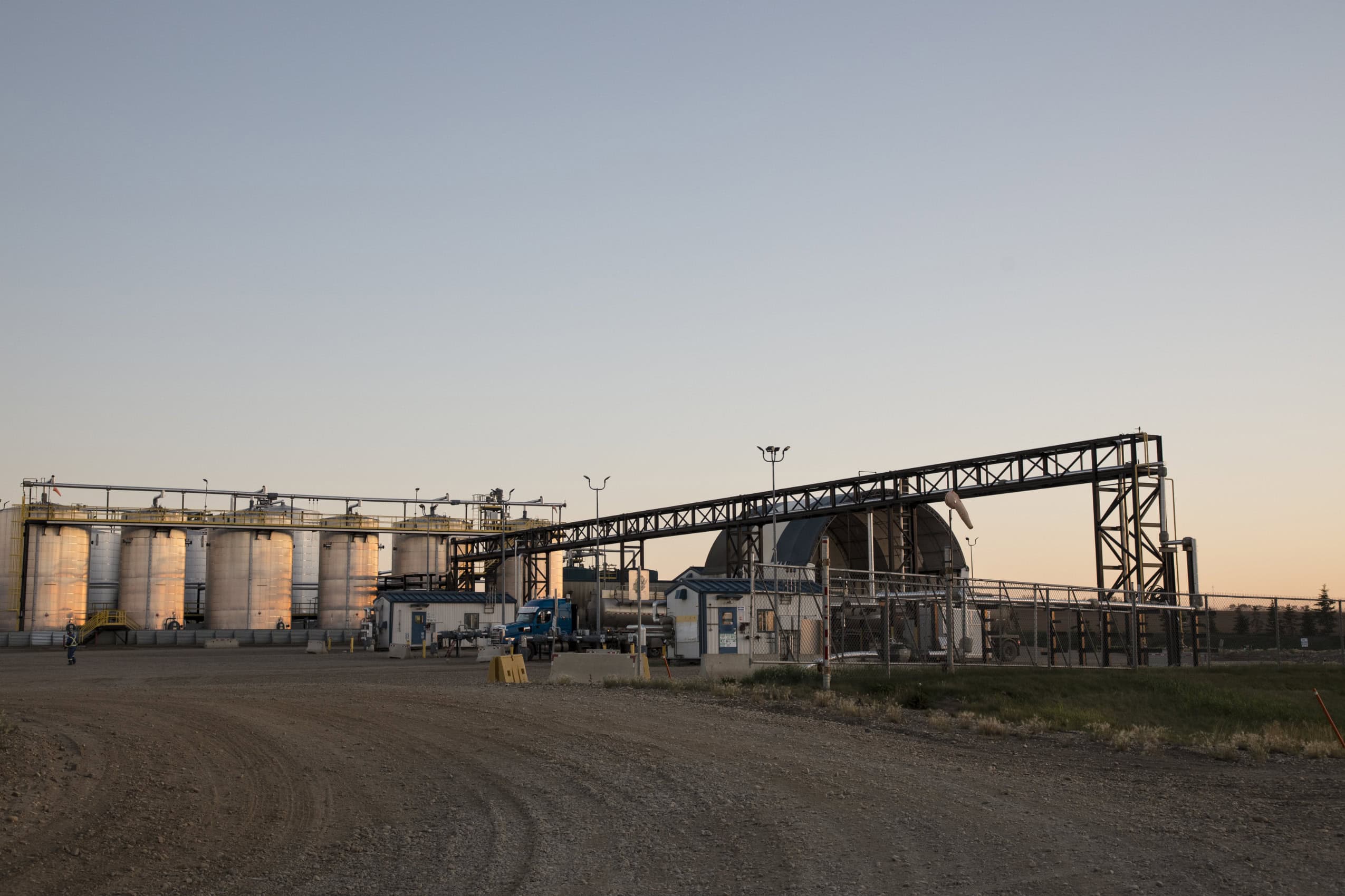 A shot of Secure's waste disposal facility at dusk. Taken from just outside the facility, looking through the open gate into the gravel lot. There are several large tanks at the back of the facility a