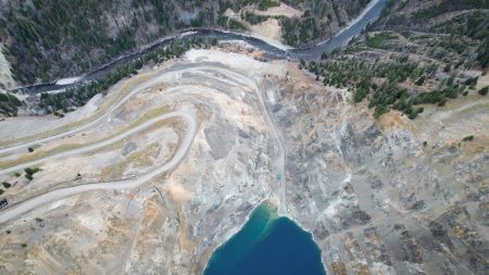 An aerial view of an open-pit mine and tailings pond with a river beside them.