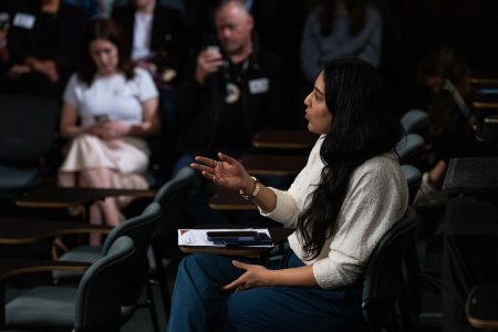Fatima Syed, sitting in a row of seats, gestures as if asking a question