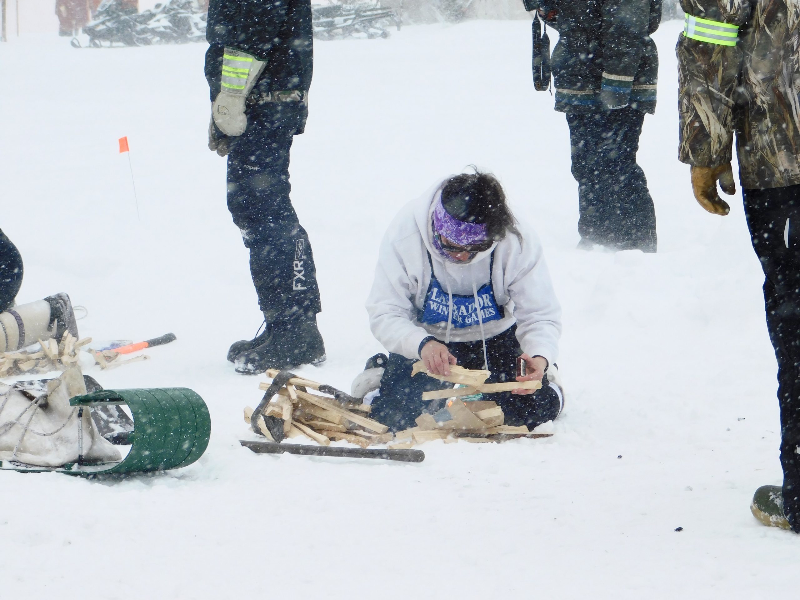 A woman kneels on the snow to start a fire