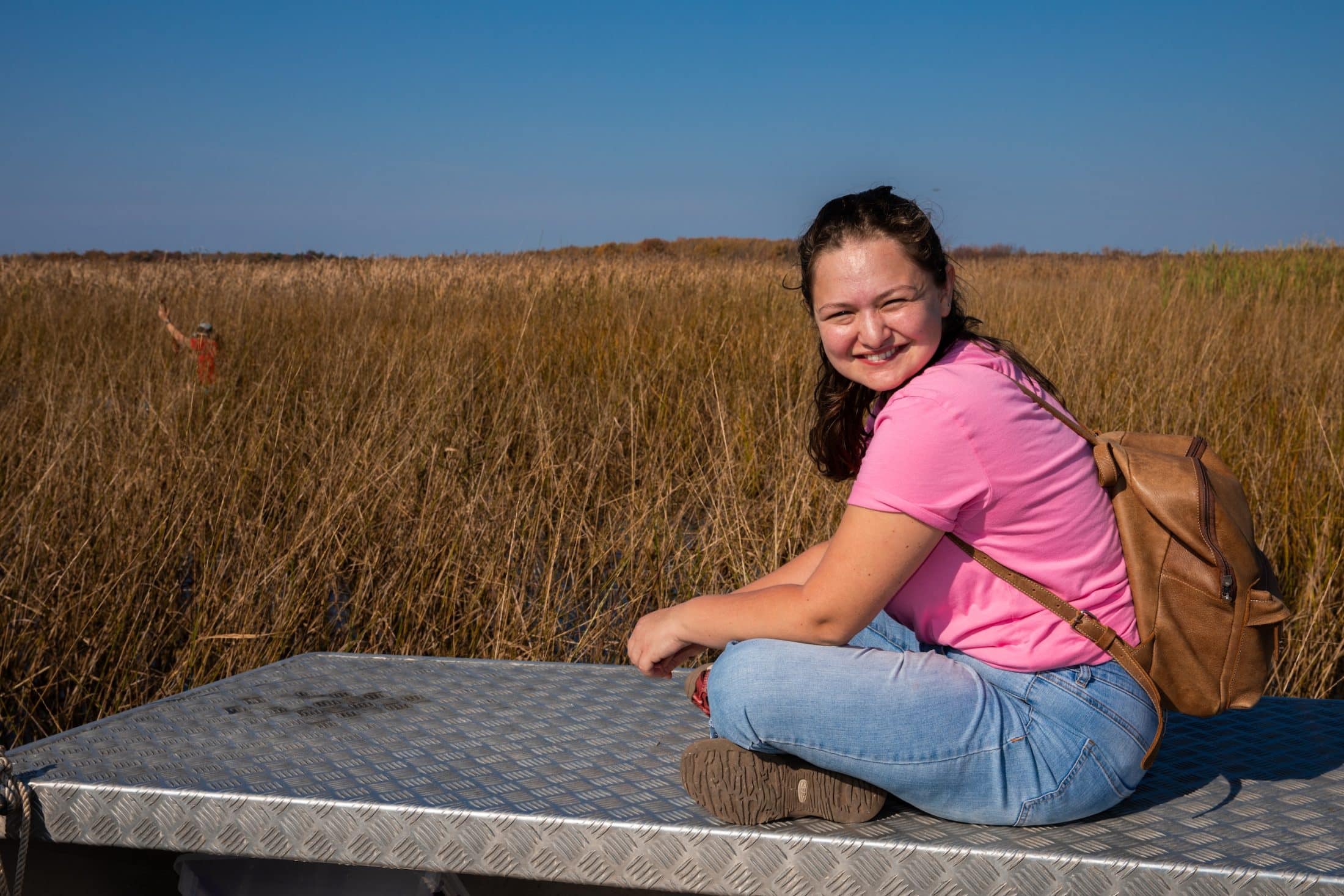 Reporter Leah Borts-Kuperman sits cross-legged in front of a field of wild rice.