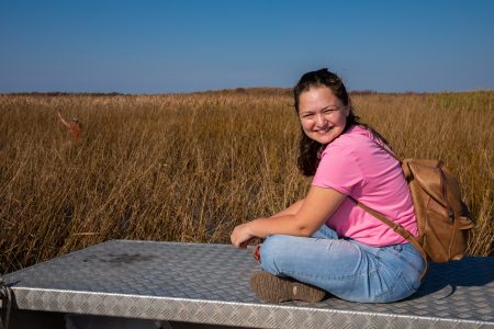 Reporter Leah Borts-Kuperman sits cross-legged in front of a field of wild rice.