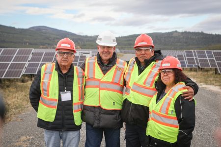 Four people in yellow vests and hard hats in front of a large array of solar panels