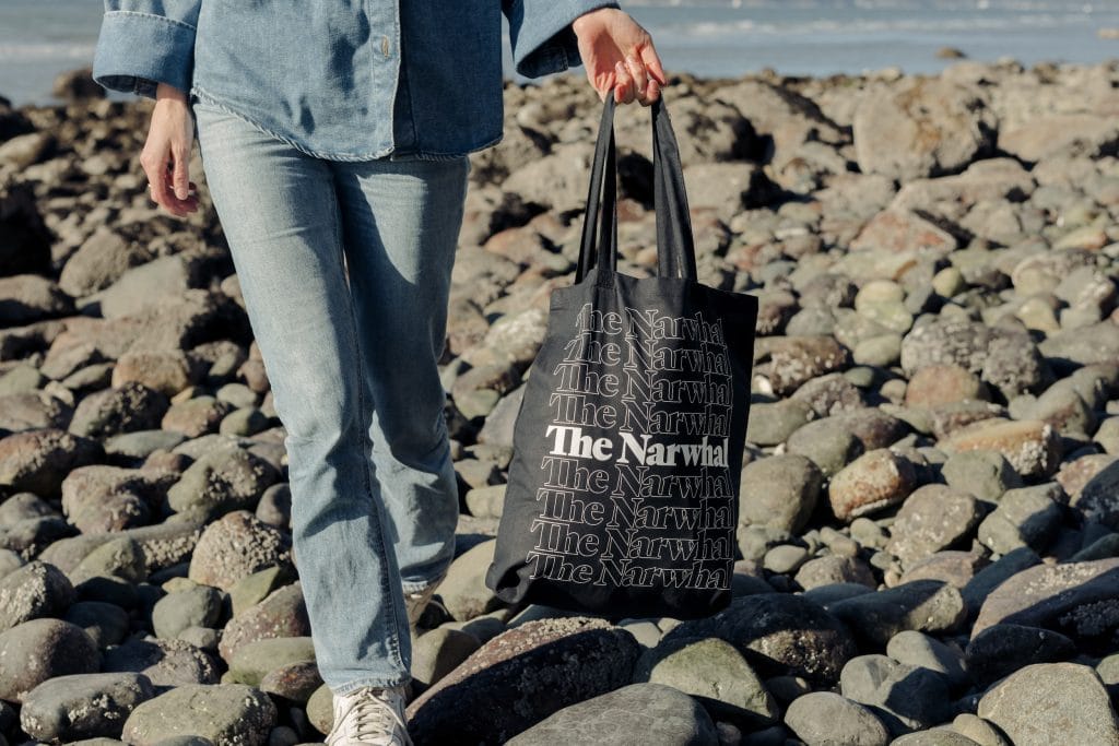 A person on a beach holds a black, Narwhal-branded tote bag