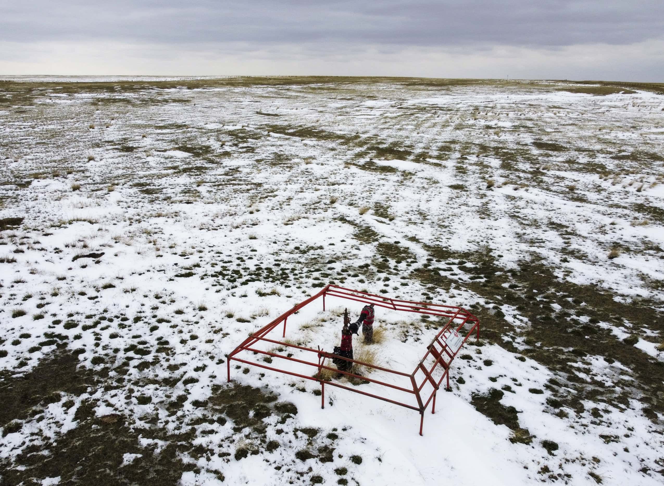 Oil and gas infrastructure in a rural Alberta field in early spring, with snow partially covering the ground.
