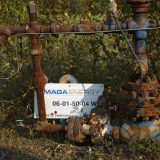 A MAGA Energy sign sits against an rusted old well site, surrounded by plants.