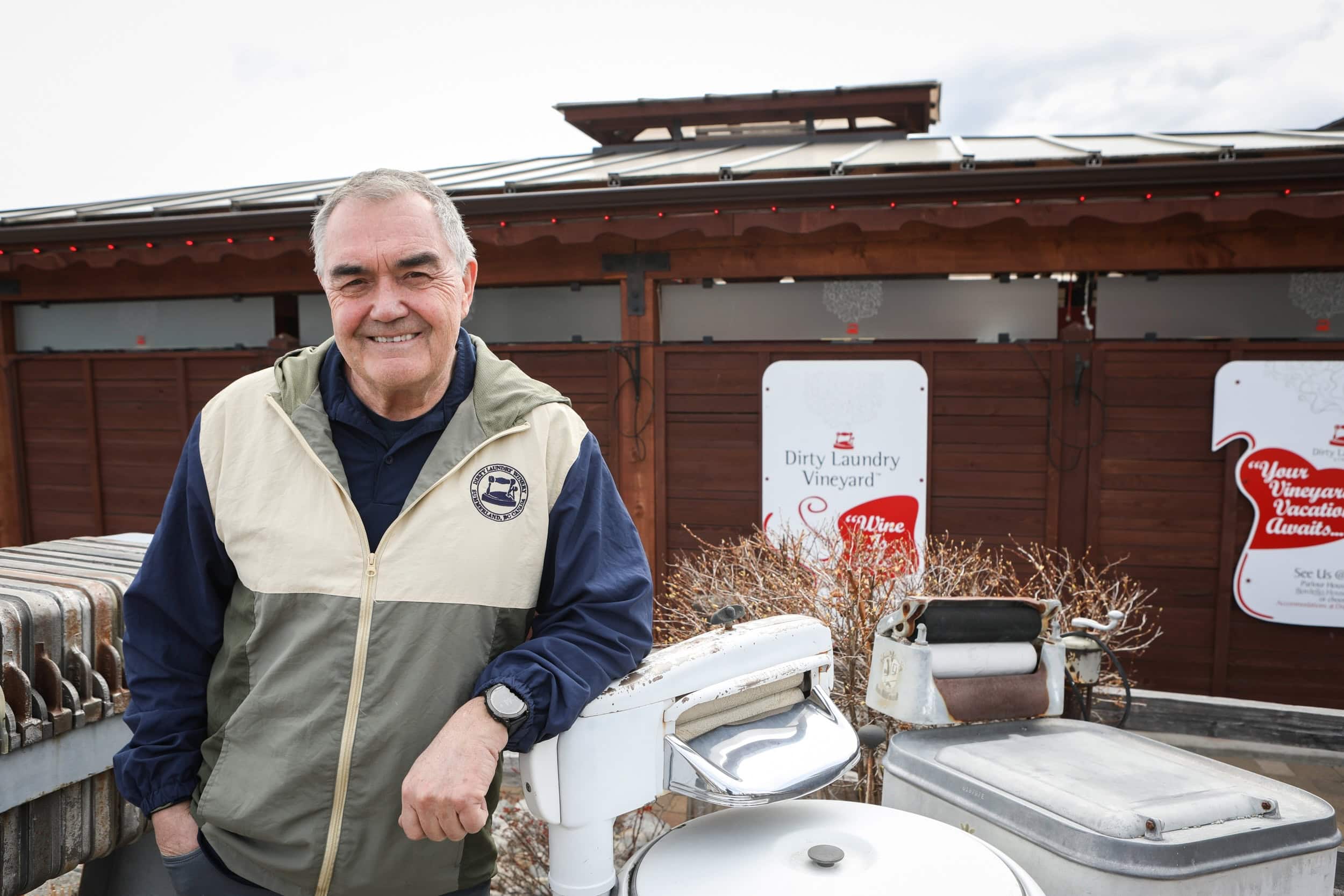 A man in a light jacket poses in front of a building with signs for Dirty Laundry Vineyard