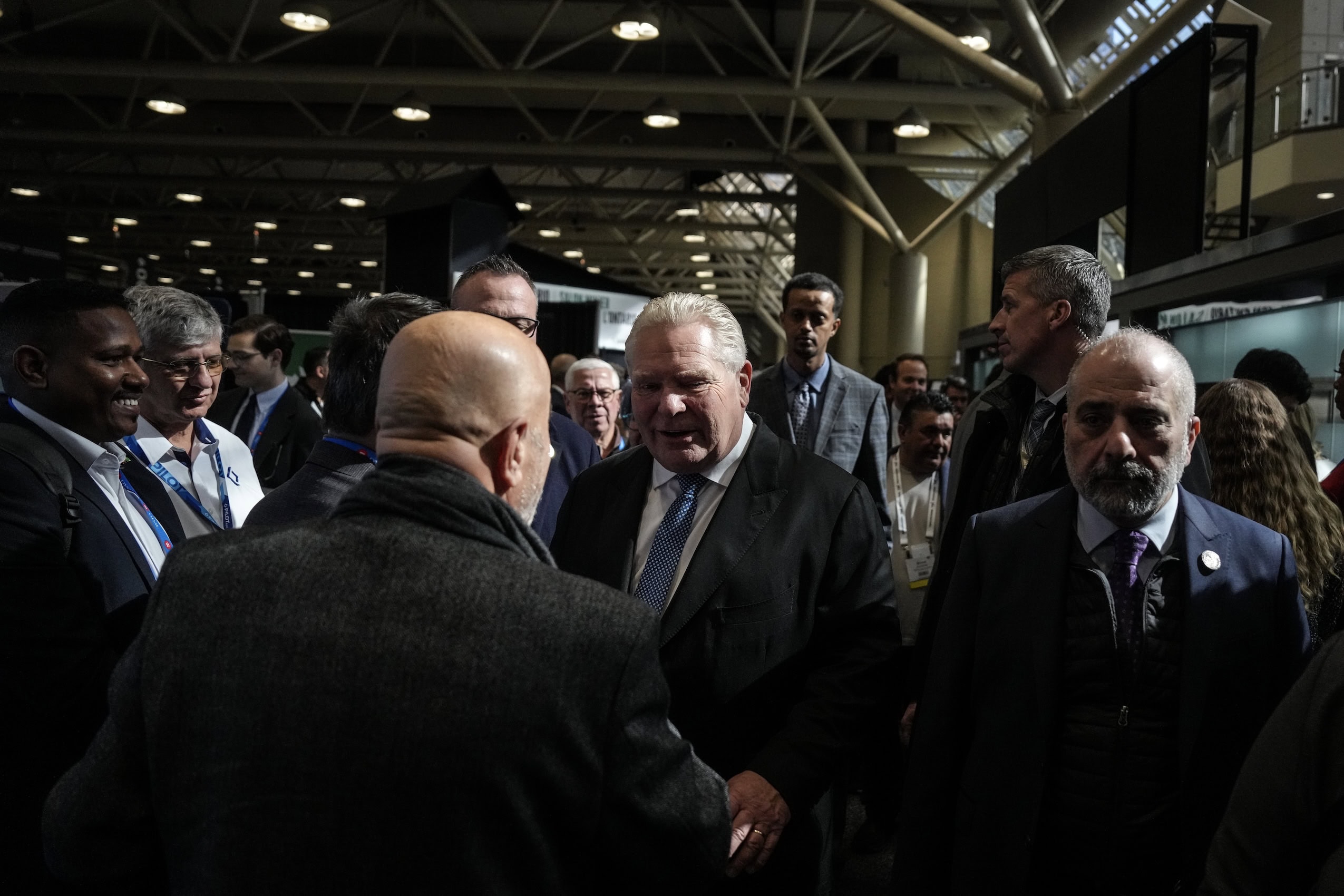 Ontario Premier Doug Ford greets an attendee on the floor of a busy conference centre.