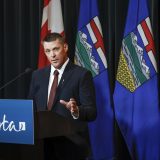 Alberta Finance Minister speaks at a lectern during a news conference, with Canadian and Albertan flags behind him.
