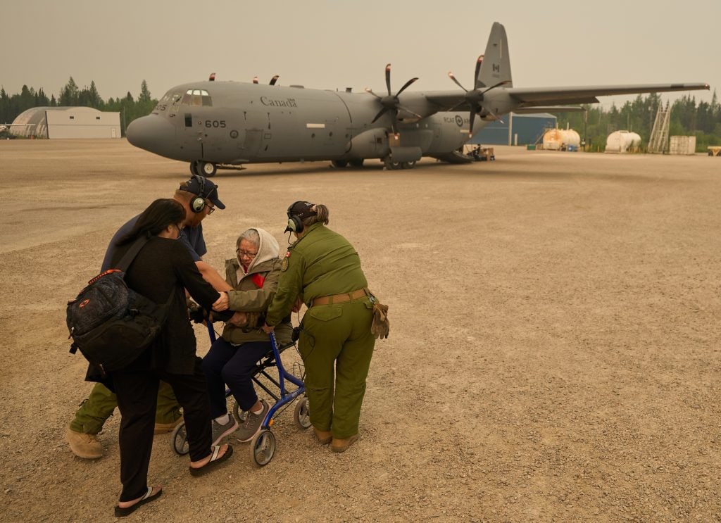 Royal Canadian Air Force members help an two wildfire evacuees as they approach an aircraft.