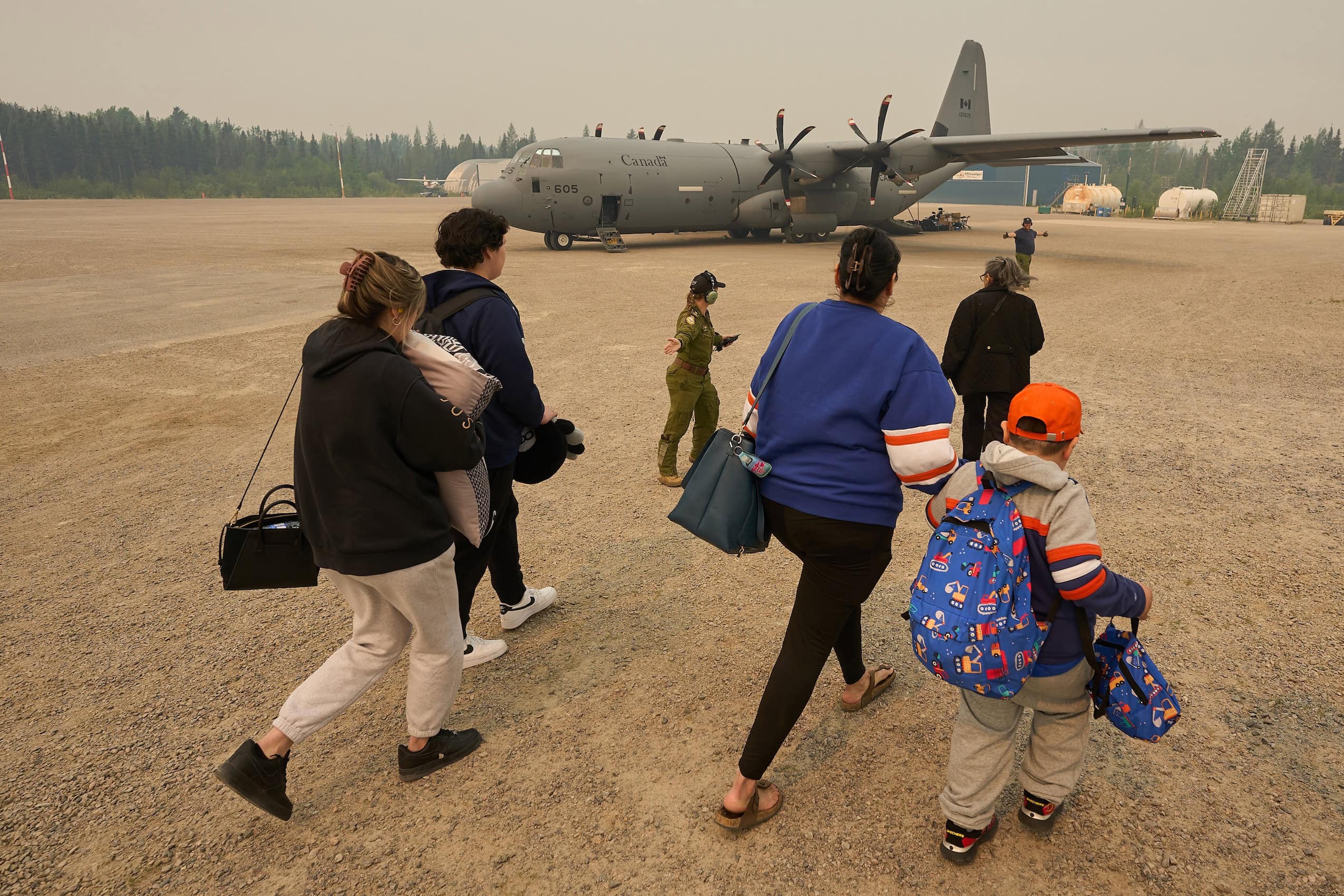 A Royal Canadian Air Force member guides a family toward a waiting aircraft during a wildfire evacuation.
