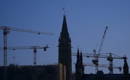 The Peace Tower on Parliament Hill is surrounded by construction cranes and silhouetted against a blue sky. Constructions cranes