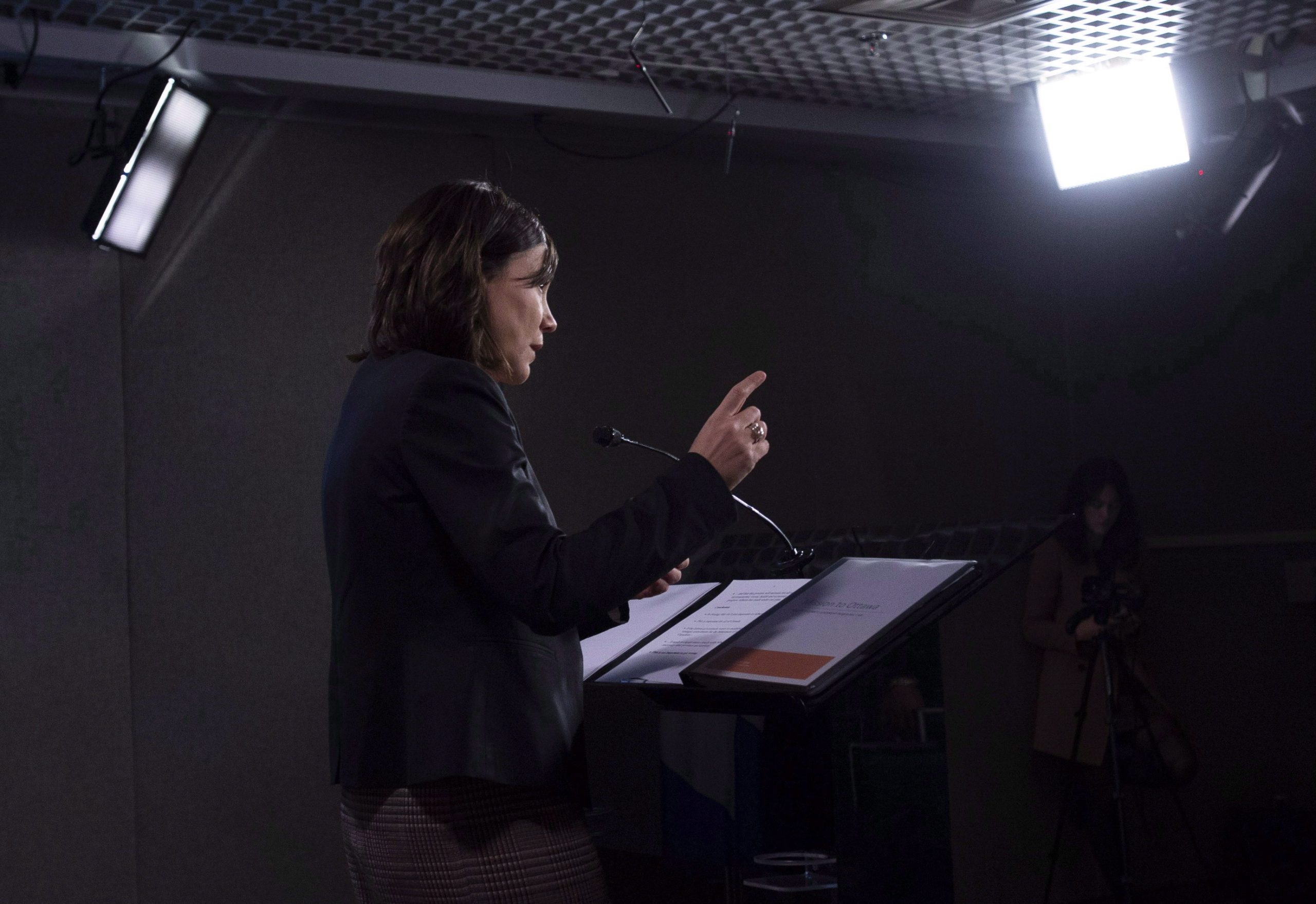 Alberta's environment minister, Shannon Phillips, speaks at a lectern under bright lights.