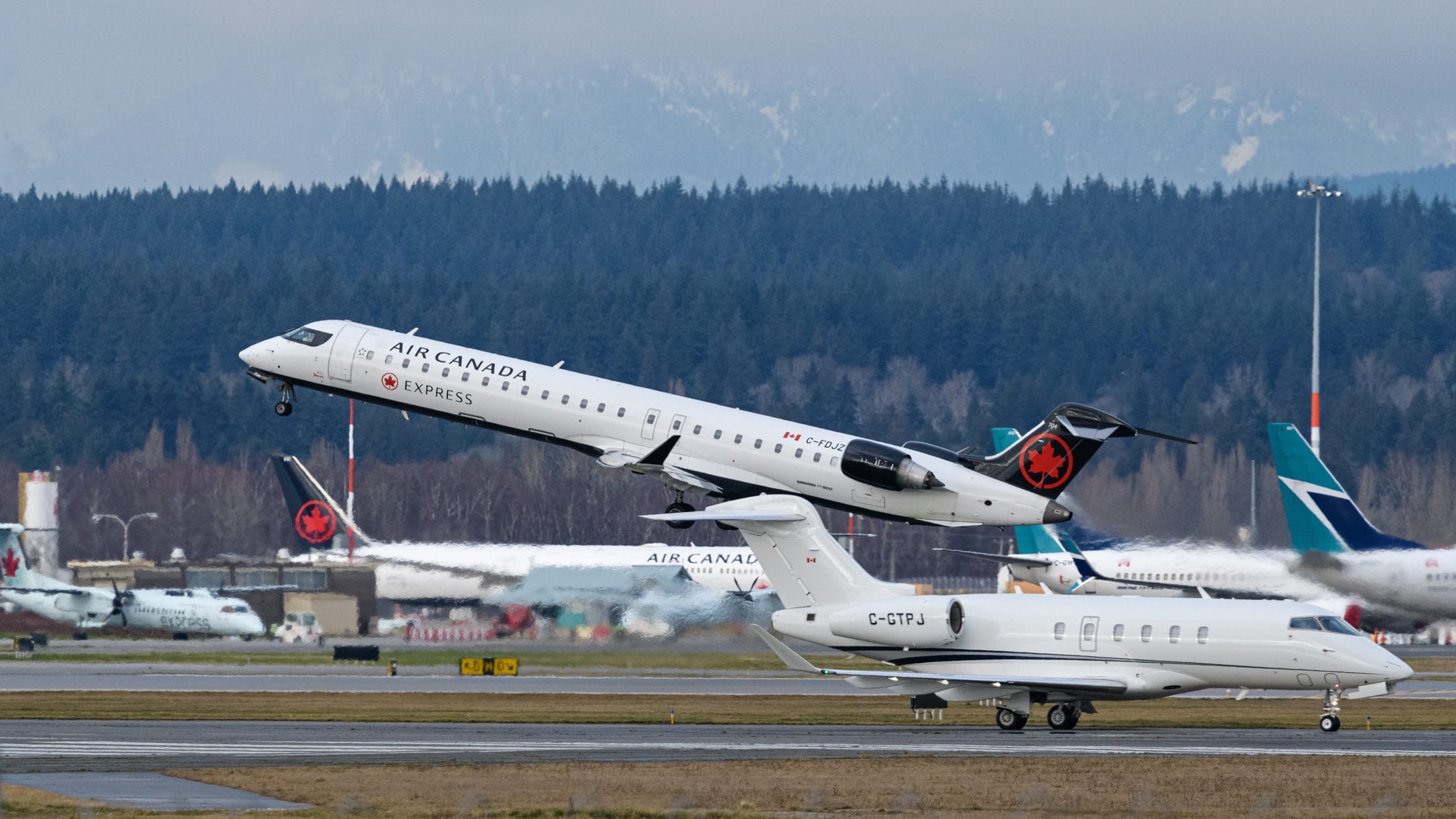 An Air Canada airplane takes off from a tarmac with other airplanes on it.