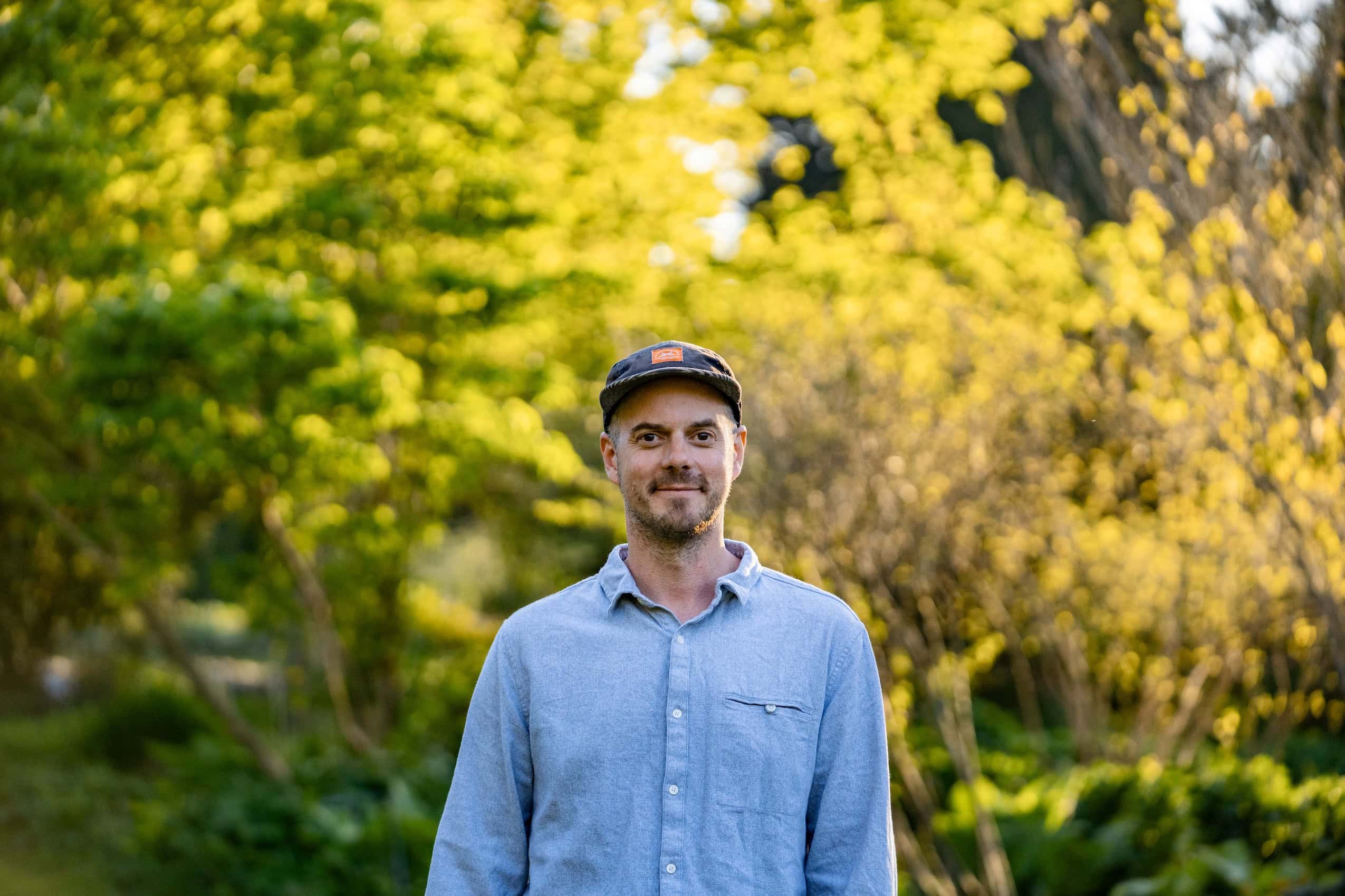 Matt Simmons, a journalist with The Narwhal, poses for a portrait, with golden sunlight illuminating trees behind him.
