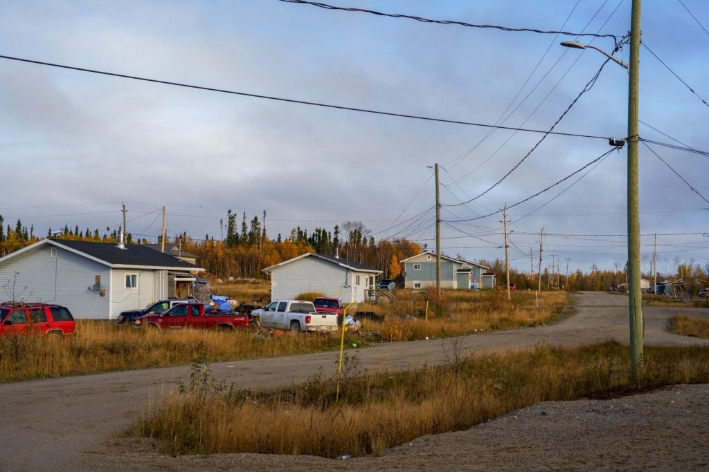 Houses, telephone poles and wires, and an empty gravel road are seen in in the remote community of Neskantaga First Nation.