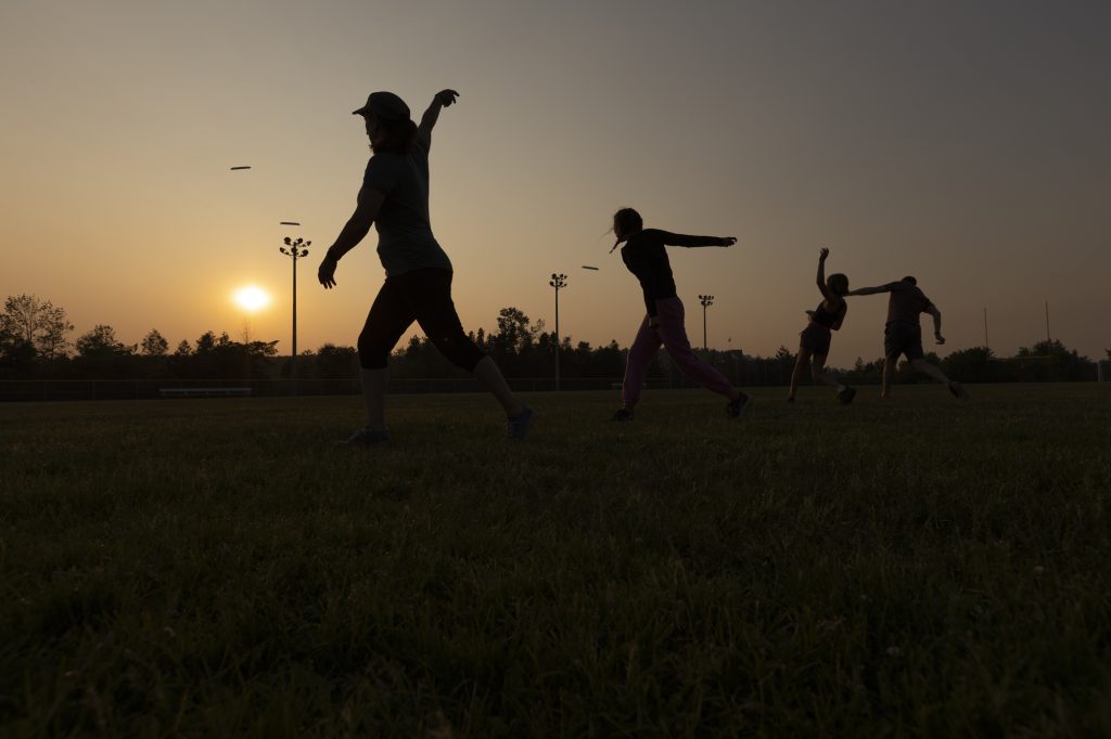 Four people throwing frisbees, silhouetted by a setting sun.