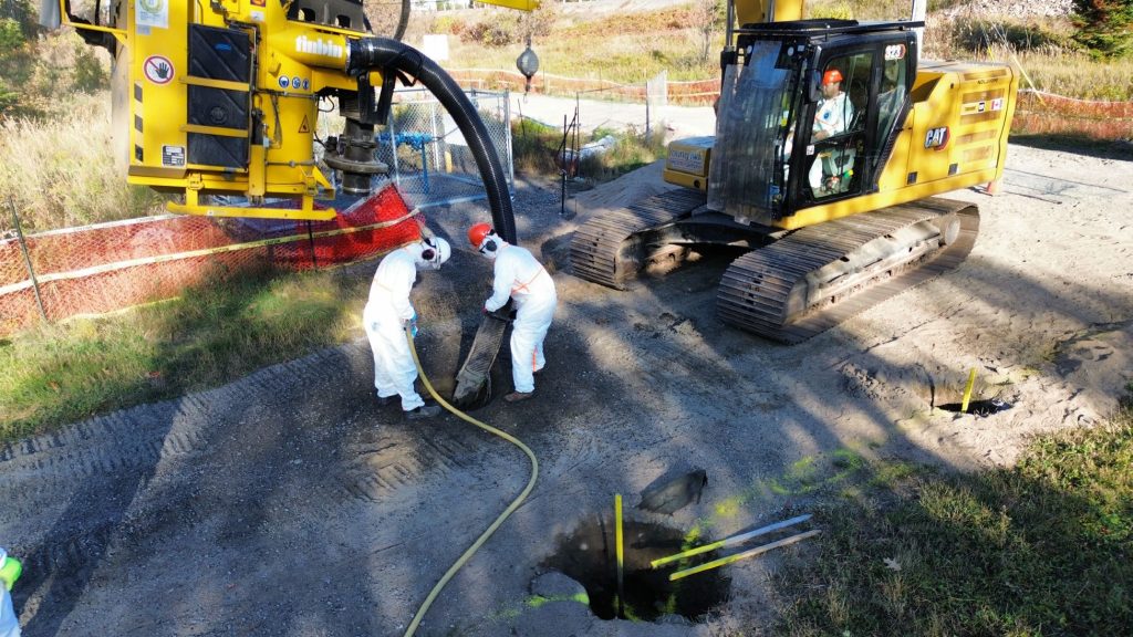 Workers in hazmat suits work to excavate and remediate niobium mine waste on Nipissing First Nation, surrounded by heavy machinery