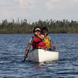 Two people in a canoe paddle toward the camera on the Seal River in northern Manitoba.