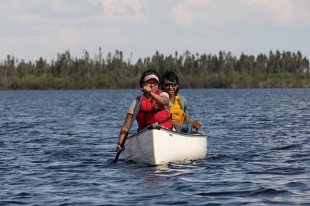 Two people in a canoe paddle toward the camera on the Seal River in northern Manitoba.