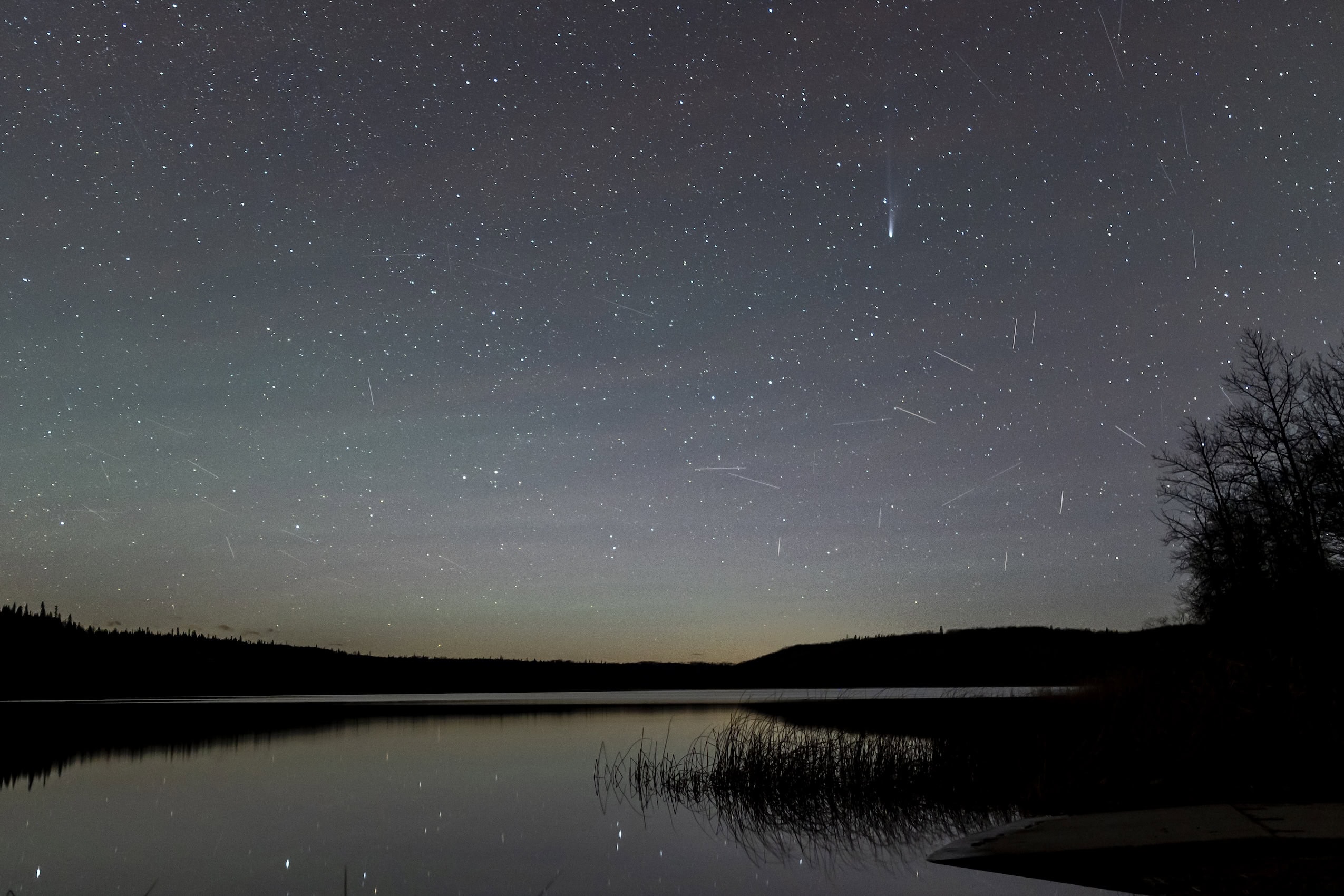 Stars light up the night sky, with a quiet lake in the foreground.