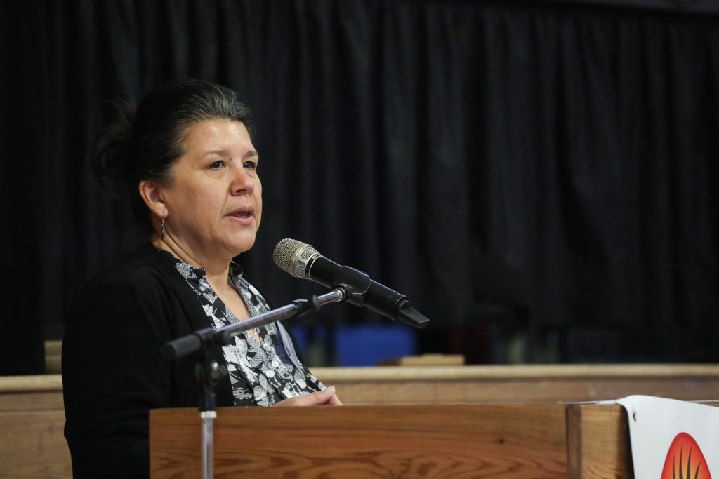 A woman stands in front of a podium addressing the crowd.