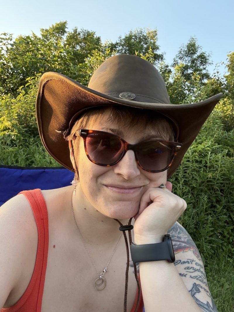Chelsea Mazur sits in a camping chair and smiles wearing sunglasses.