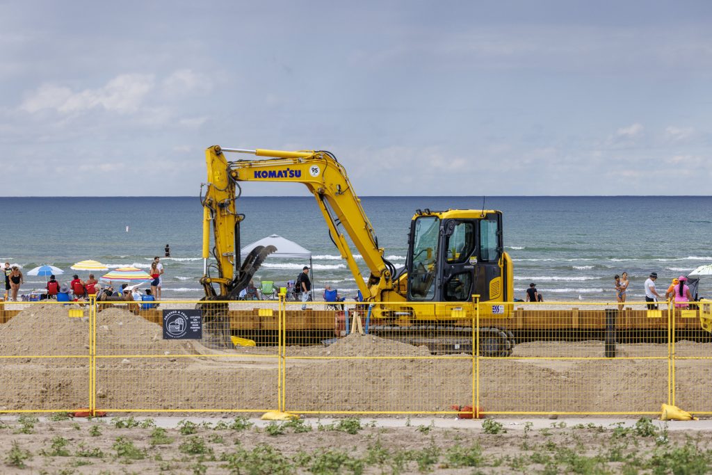 Bright yellow construction equipment sits idle on Wasaga Beach while bathers enjoy the beach.