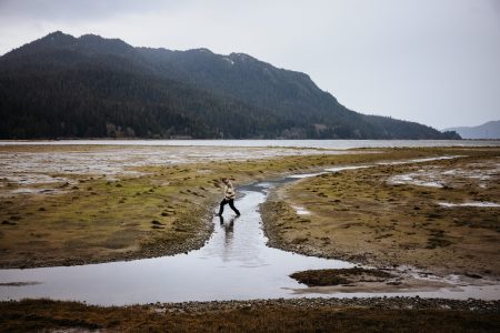 A man walks through a stream, dwarfed by an expansive landscape.