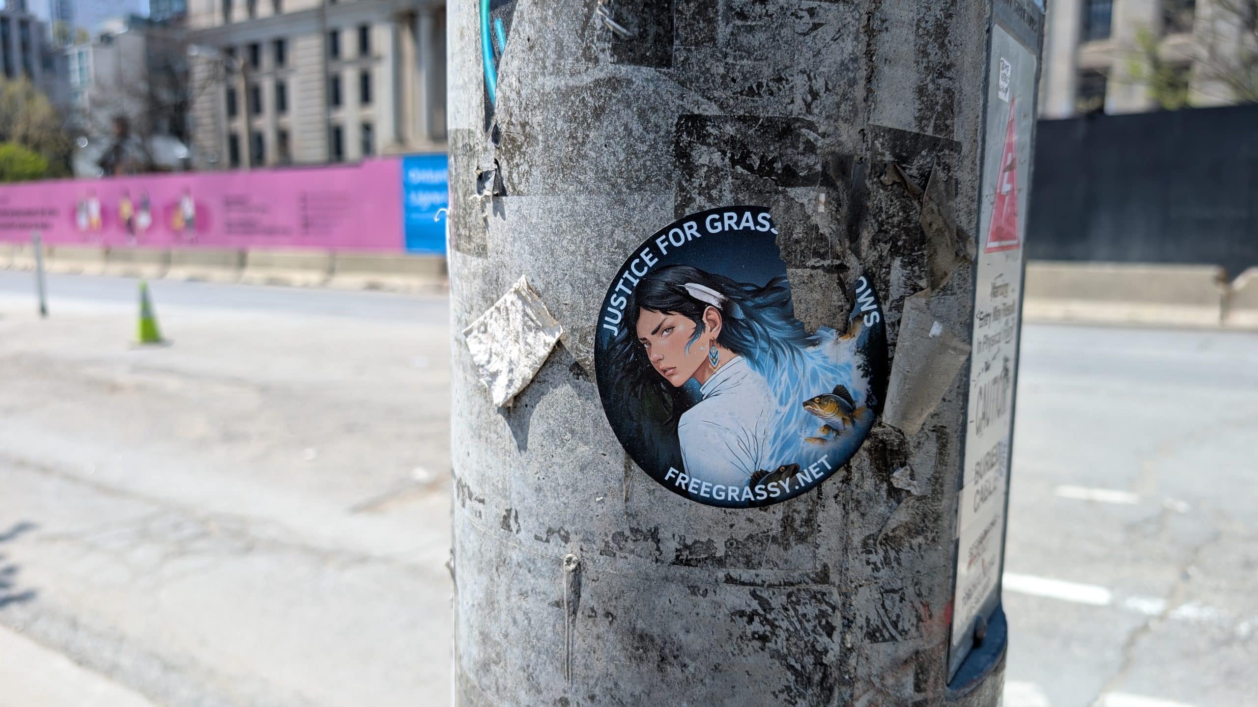 A sticker on a pole of a woman with the words Justice For Grassy Narrows slightly ripped off the picture