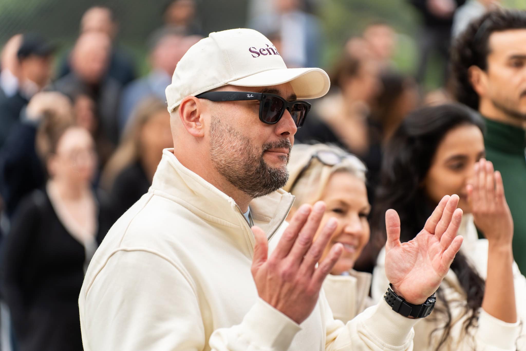 A man raises his hands, wearing a hat with sunglasses.