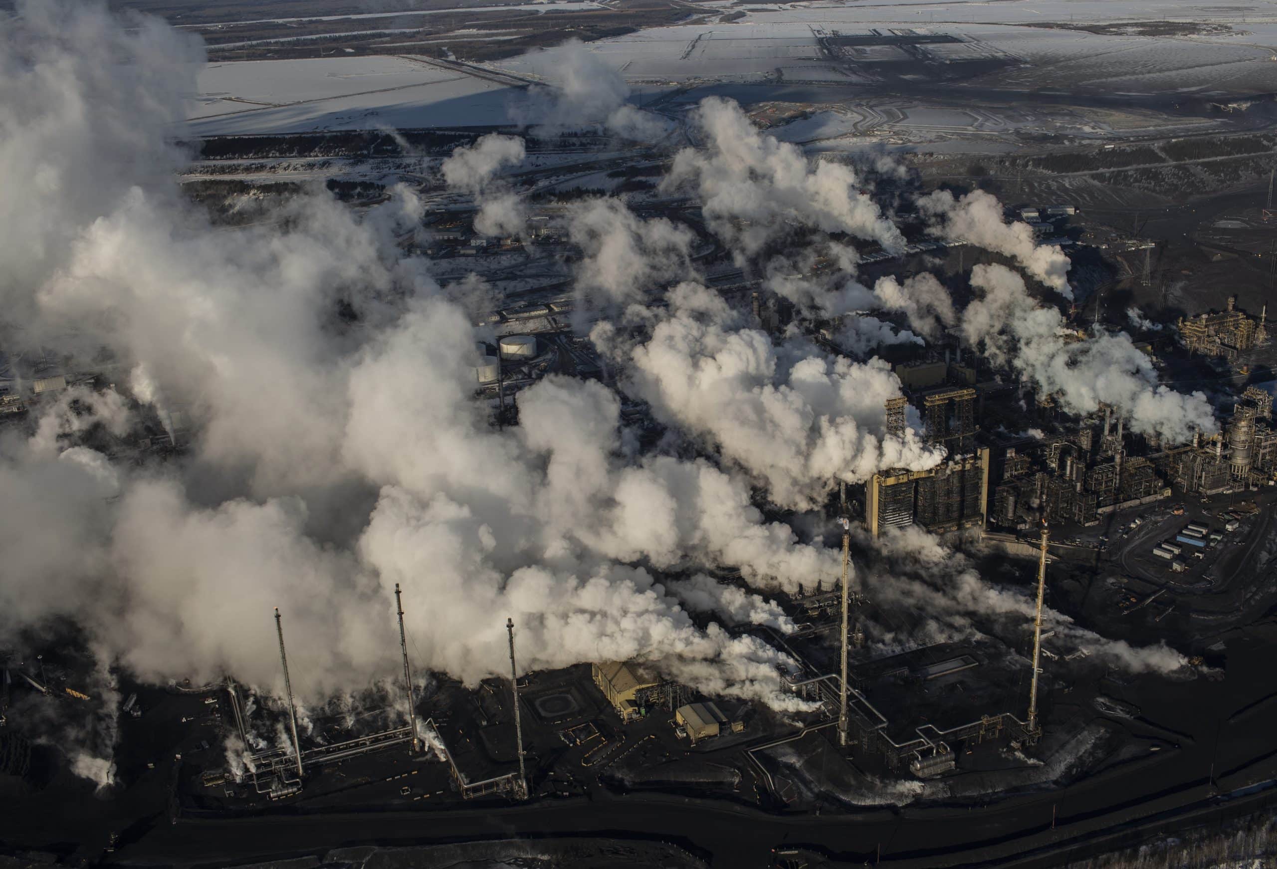 An aerial view of smoke emitting from smoke stacks in Alberta's oil fields on a sunny day.