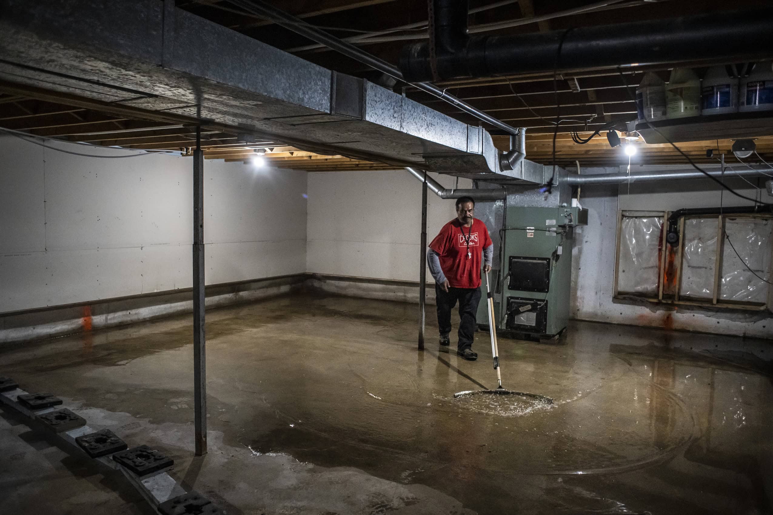 A man mops up flood waters in a basement.