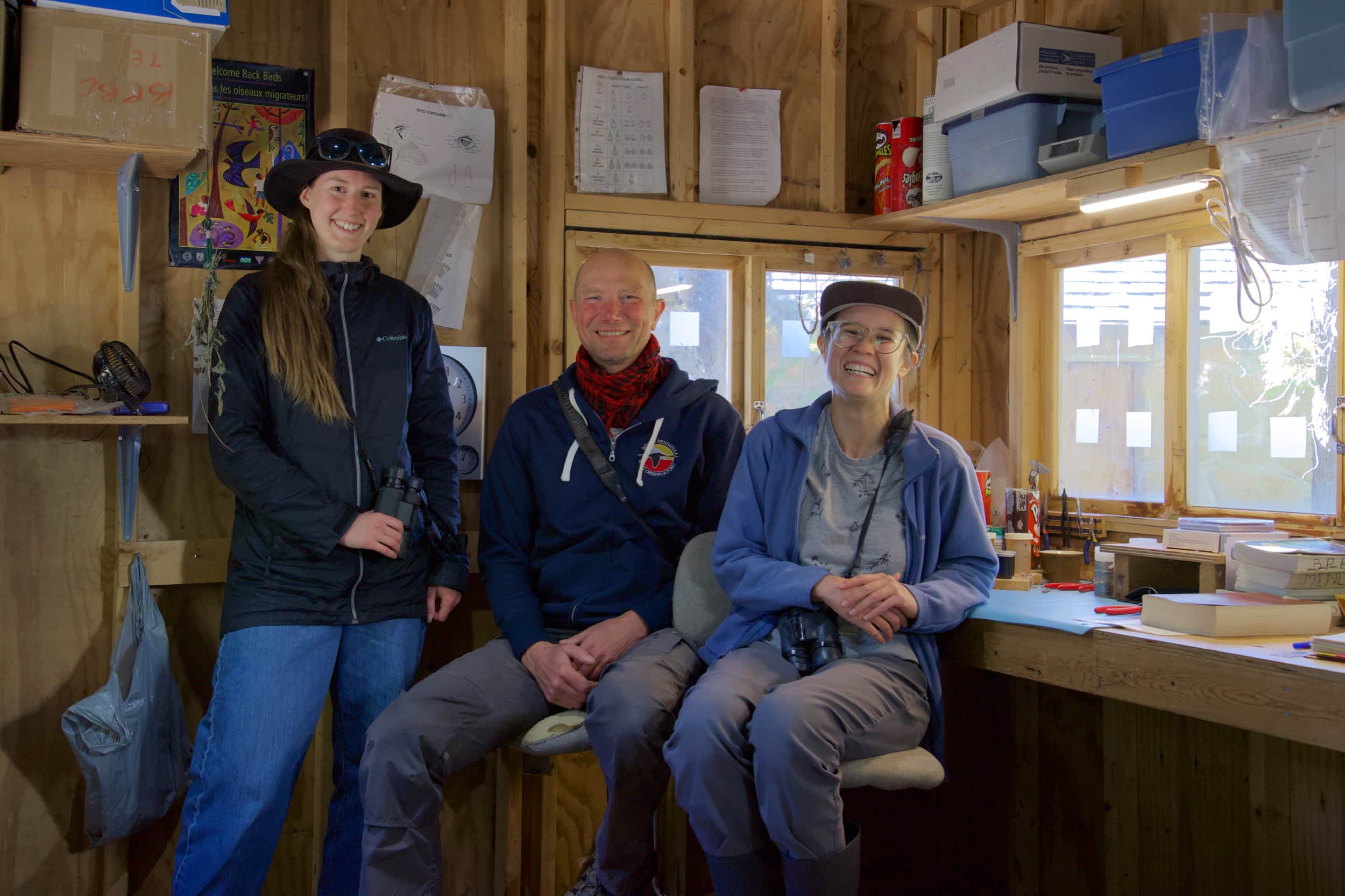 Three people in a wood cabin, smiling at the camera.