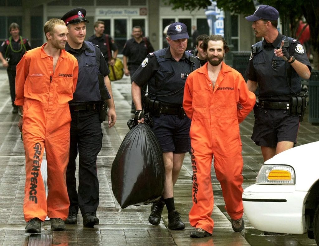 Two Greenpeace activists wearing orange jumpsuits, including Steven Guilbeault who later became Canada's environment minister, are led away by police officers in 2001.