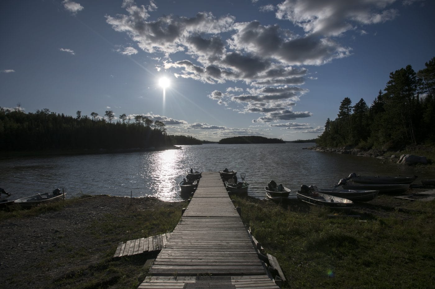 A dock with boats around it leads out into sparkling waters under a blue sky