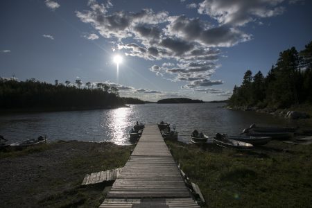 A dock with boats around it leads out into sparkling waters under a blue sky.