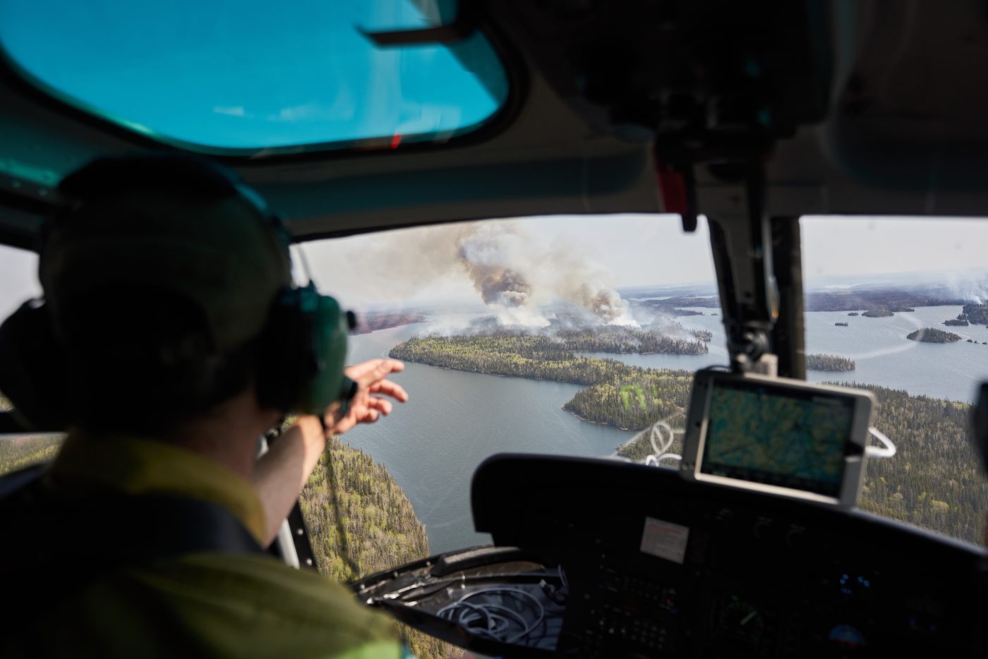 A man in a helicopter points out towards an island with smoking rising from its forests.