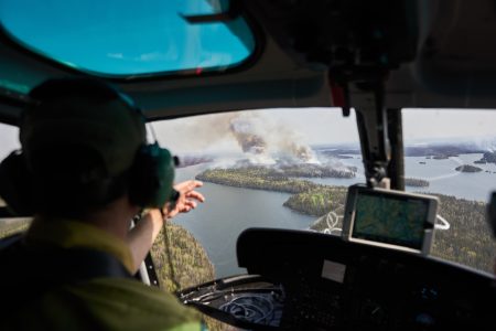 A man in a helicopter points out towards an island with smoking rising from its forests.