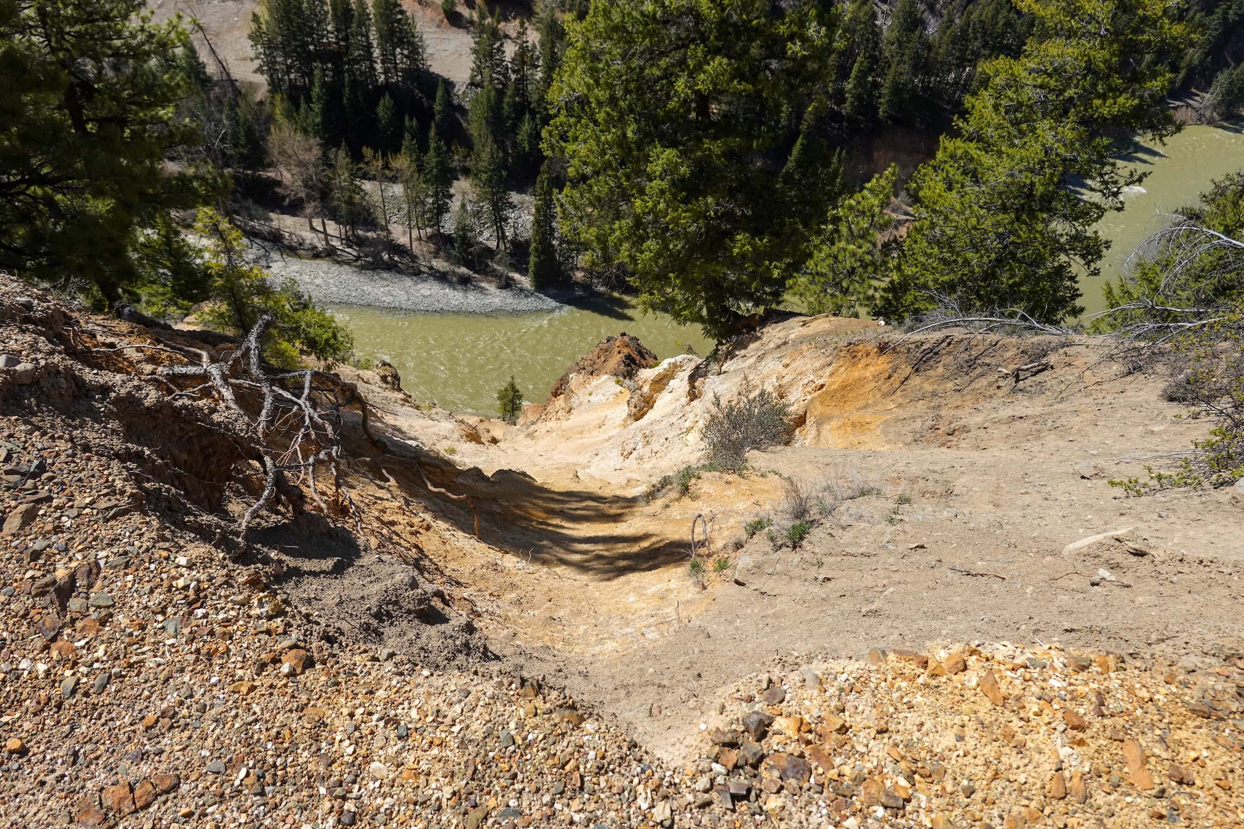 A hillside gully leading into a muddy river.